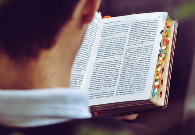 Man reading a text book with numerous pages tagged with stickynotes