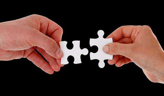 Two hands holding two separate jigsaw pieces which connect together exactly